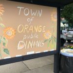 A large chalkboard with 'Town of Orange public Dining' written on it. There are also drawings of flowers on the board as decoration.