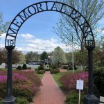 An outdoor photo of the Memorial Park in Orange. At the centre of the photo is a metal garden arch with the name of the park at the top. It leads into the garden where the Peace Statue is.